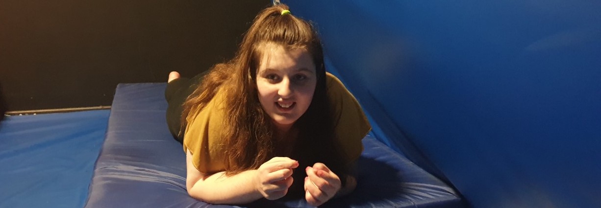 A smiling girl lies on a blue mat in a sensory room