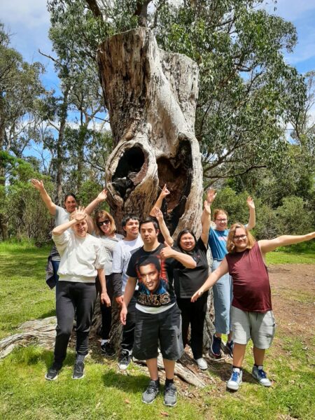 Group of people standing in front of a very large tree, smiling at the camera